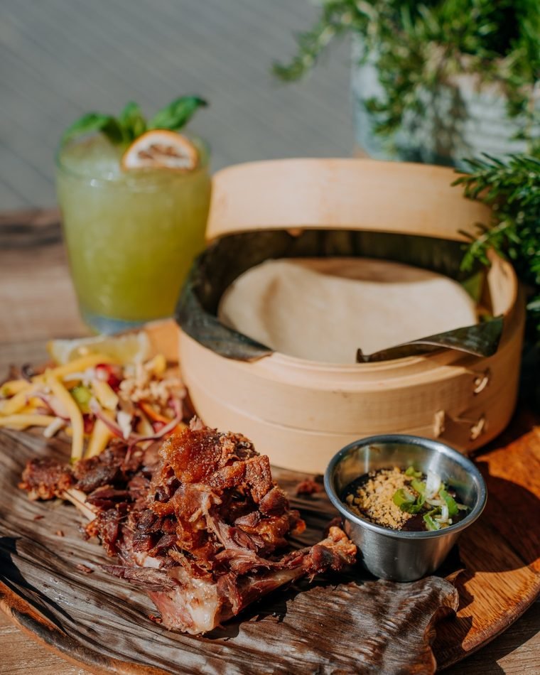 Duck Yourself: pato confitado desmenuzado sobre una tabla de madera, con vaporera de bambú, ensalada de mango y chili y salsa hoisin.